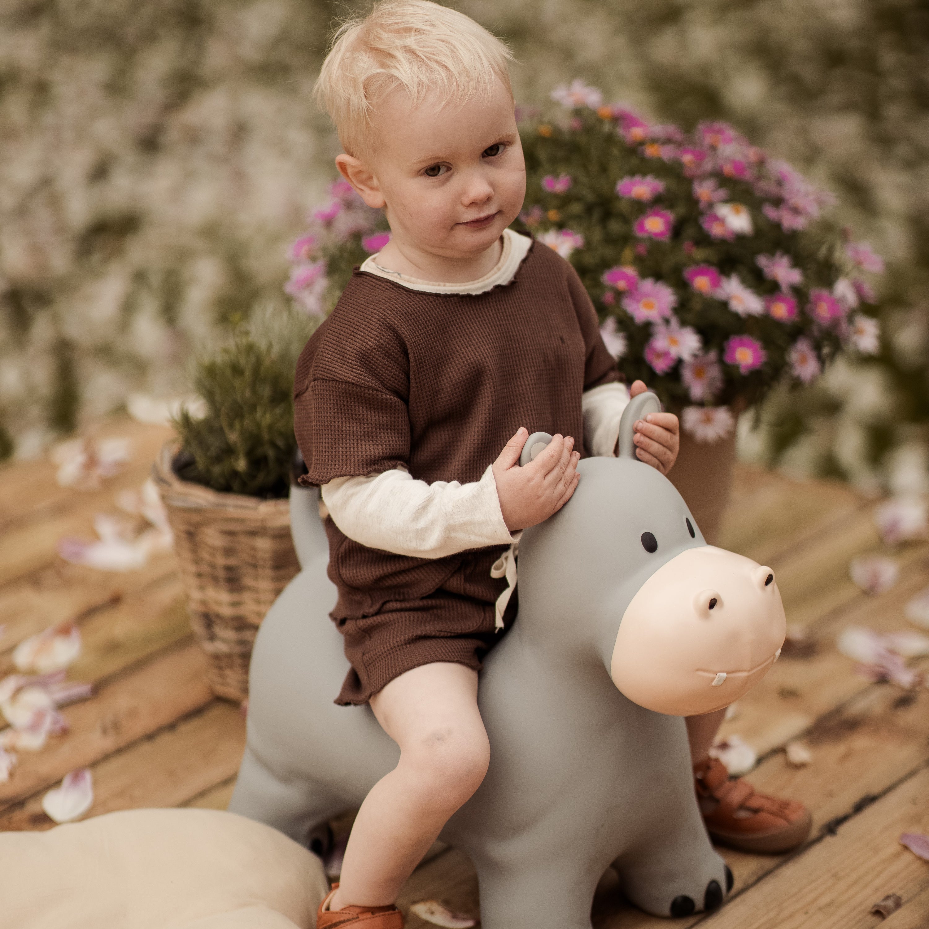 Child sitting on Holger the light grey bouncing hippo toy in a flower-filled setting – Find That Hippo