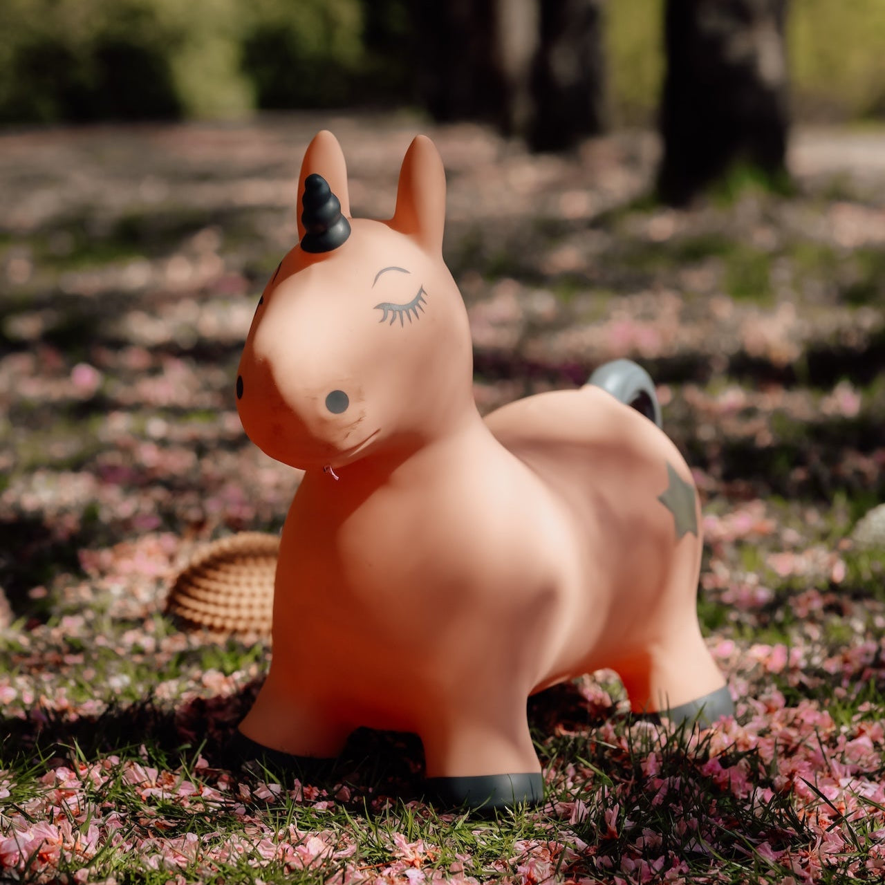 Luna the Unicorn, a pink inflatable jumping toy, outdoors on a path covered in pink petals.