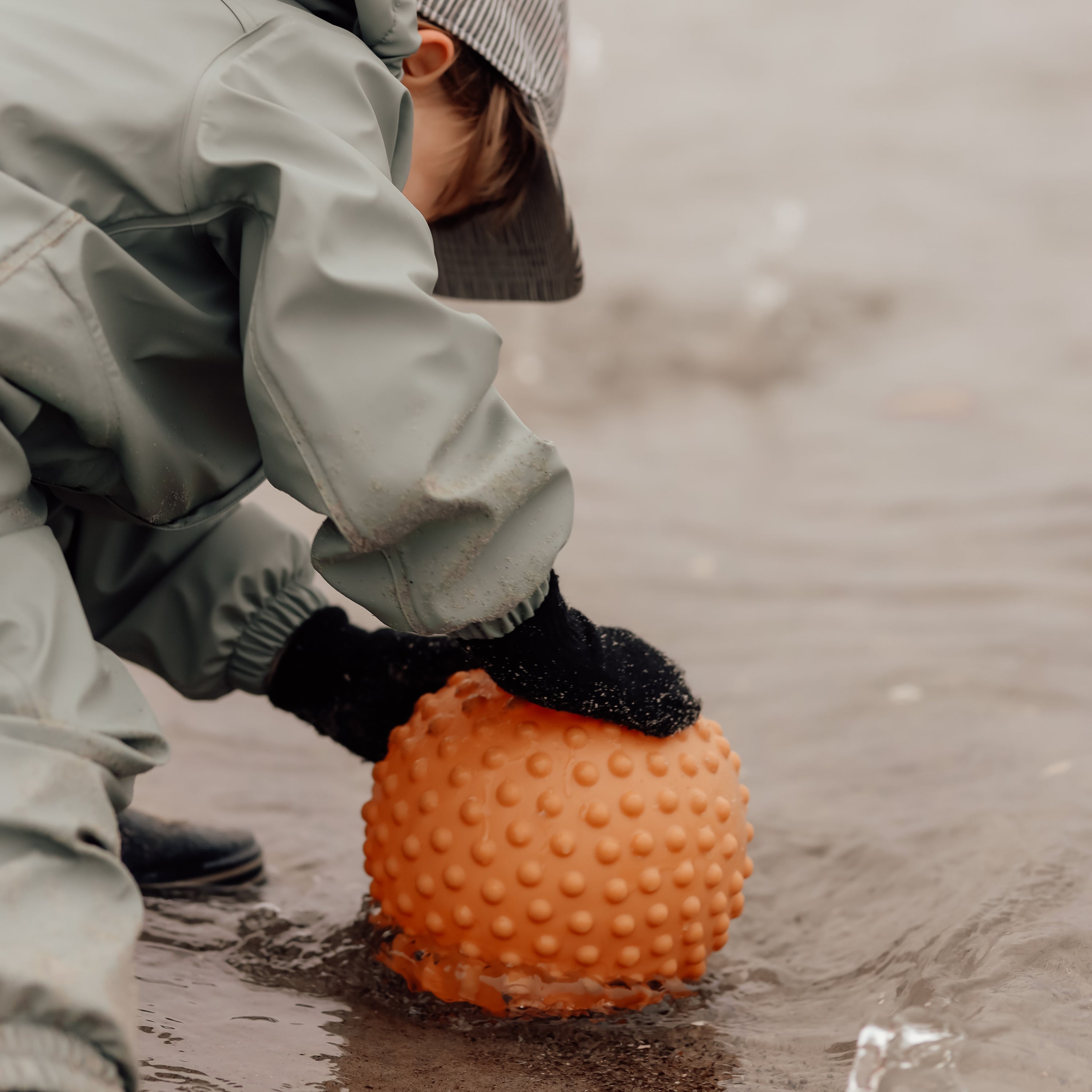 Child kneeling on sand next to a muted orange sensory ball – Find That Hippo