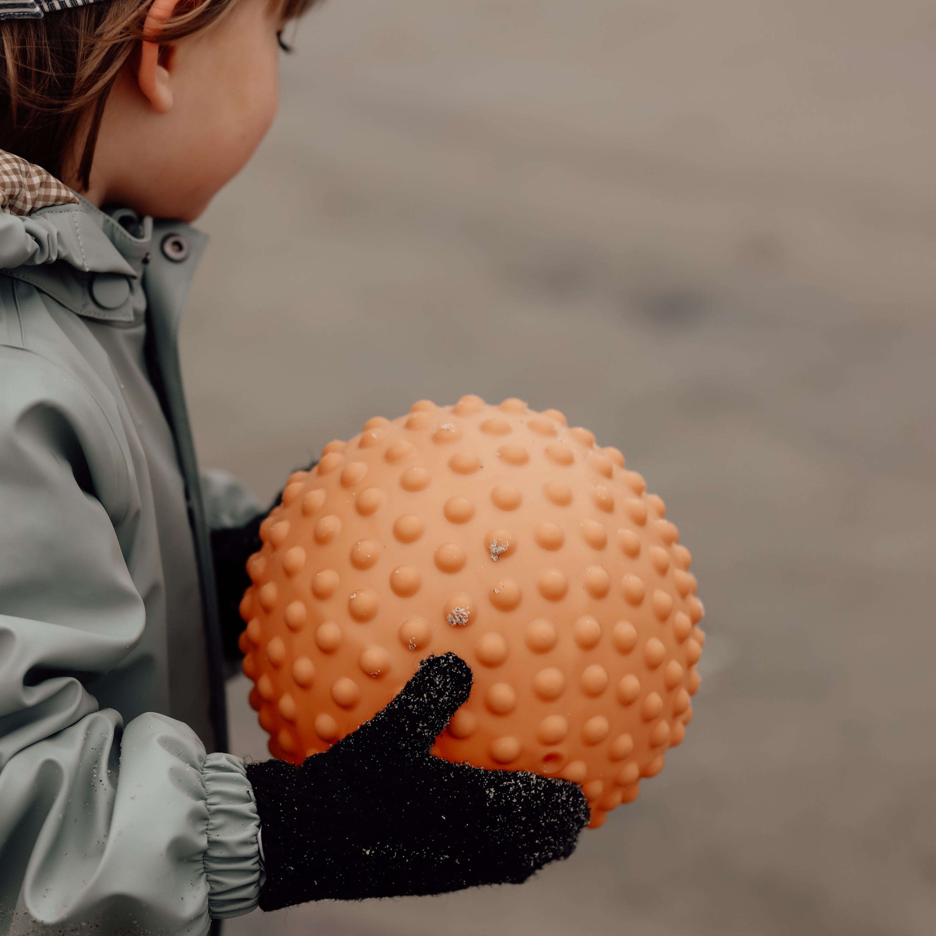 Child playing outdoors with large muted orange sensory ball in their hands – Find That Hippo
